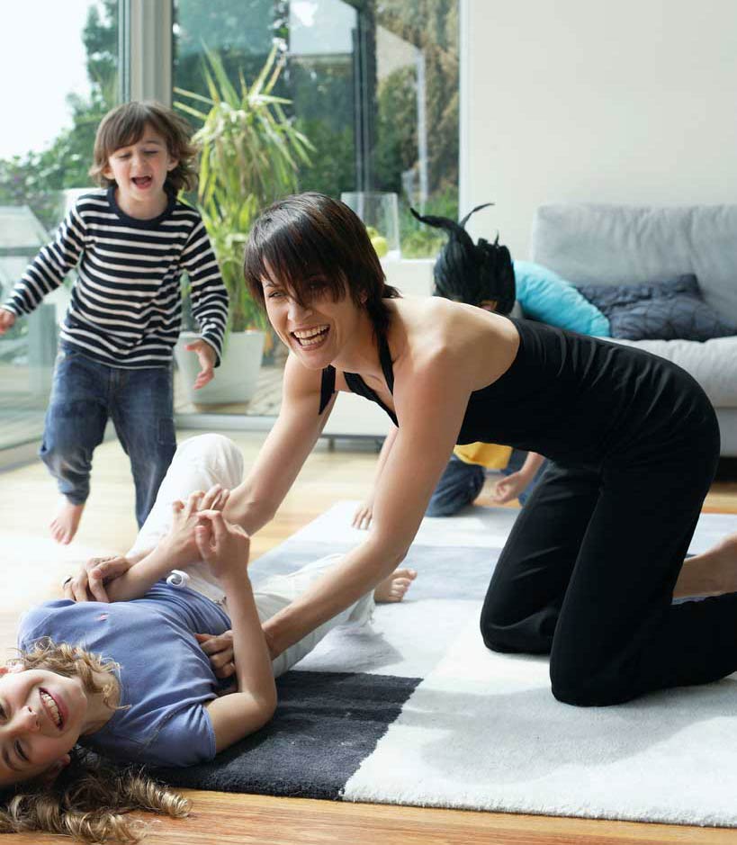 Hip boho Mom in yoga clothes playing with her kids in her modern, luxury living room
